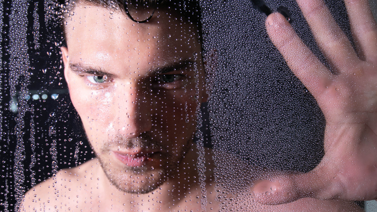 Portrait of handsome man with green eyes looking out from behind rainy glass or shower cubicle.