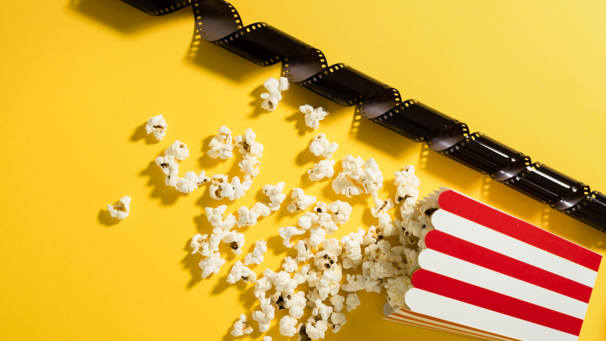 Classic striped bucket with delicious popcorn and film stock on yellow background.